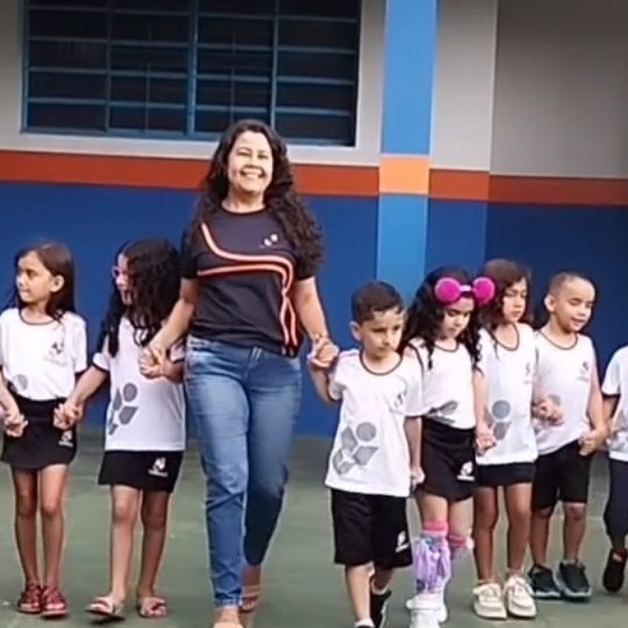 Professora do CEDULC caminhando de mãos dadas com alunos da Educação Infantil